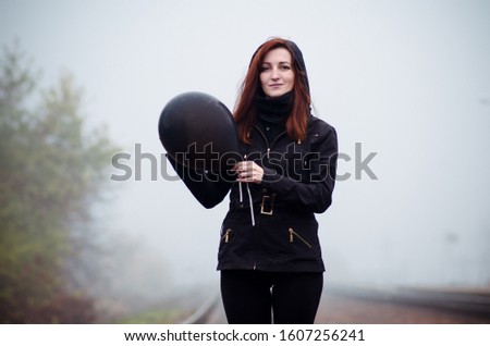 Lonely girl in black clothing walking in a fog. She holds a black balloon in her hand. Concept of choice, target, good and evil, way in life