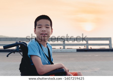 A child on wheelchair is smile happily, Amateur photographer hold camera in hand, Public Bridge background and sun rise, Life in the education age of disabled children, Happy disabled kid concept.