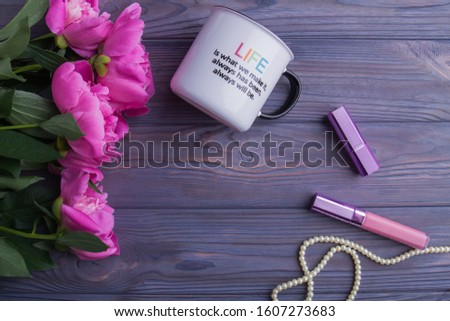 Woman's accessories on wood with copyspace. Peony flowers, cup, lipstic, mascara and pearl necklace arranged around with free space.