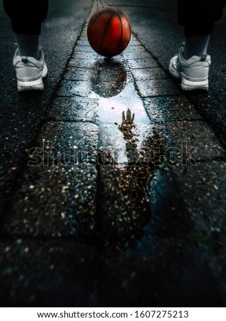 A person playing basketball in a puddle of rain, on a dark street