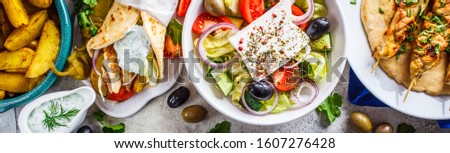 Greek food: greek salad, chicken souvlaki, gyros and baked potato wedges on gray background, top view. Traditional greek cuisine concept.