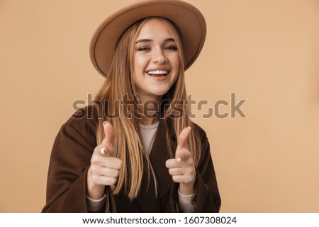 Image of young caucasian girl wearing hat and coat smiling and gesturing cool you isolated over beige background