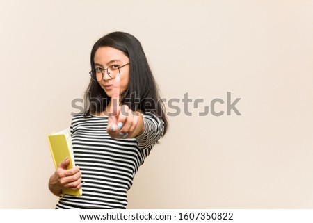 Young asian woman student holding a book showing number one with finger.