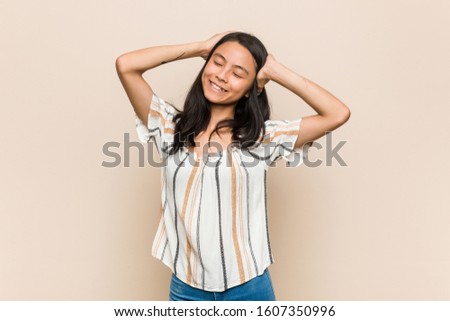 Young cute chinese teenager Young blonde woman wearing a coat against a pink background laughs joyfully keeping hands on head. Happiness concept.