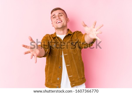 Young caucasian man isolated feels confident giving a hug to the camera.