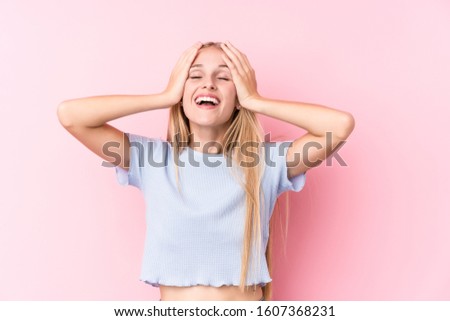 Young blonde woman on pink background laughs joyfully keeping hands on head. Happiness concept.