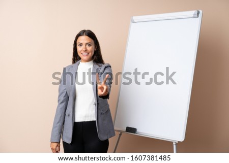 Young woman giving a presentation on white board smiling and showing victory sign