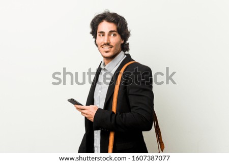 Young business man holding a phone looks aside smiling, cheerful and pleasant.