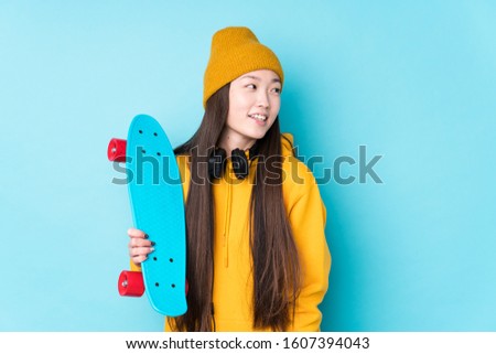 Young chinese skater woman isolated looks aside smiling, cheerful and pleasant.