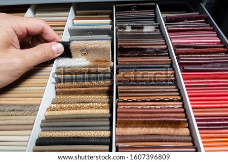 Multi-color leather in earth tone base in sample box with finger point to leather sheet / interior design / sample material