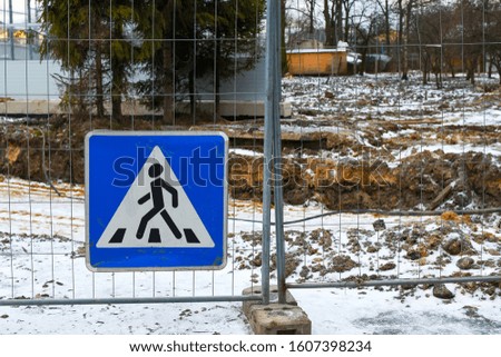 Pedestrian crossing sign on the fence on the background of construction work on the renovation of the road