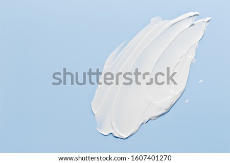 White cosmetic cream lotion moisturizer strokes on pastel blue. Hygiene, skincare product creamy texture. Beauty face creme smear smudge swatch on color background Royalty-Free Stock Photo #1607401270