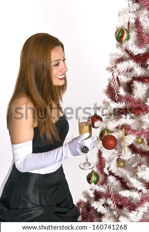 A Hispanic woman in an evening gown and white gloves, holding a glass of champagne, while looking at a decorated Christmas tree.