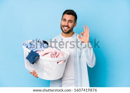 Young handsome man doing laundry isolated cheerful and confident showing ok gesture.