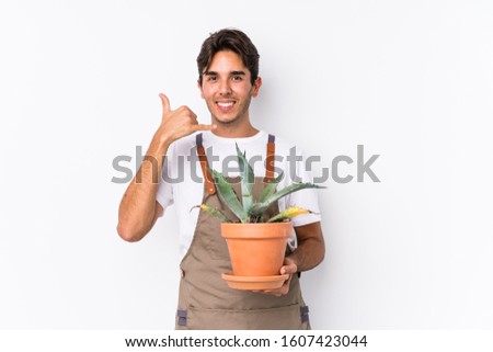 Young caucasian gardener man holding a plant isolated showing a mobile phone call gesture with fingers.