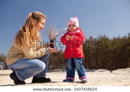 Mom and child holding willow flowers in their hands and looking at them. Photo outdoors, blurred background