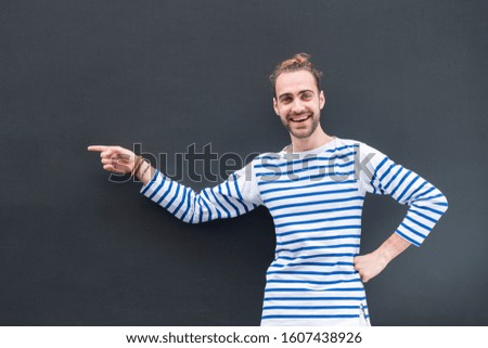 Portrait smiling man with beard pointing finger to empty space on black background