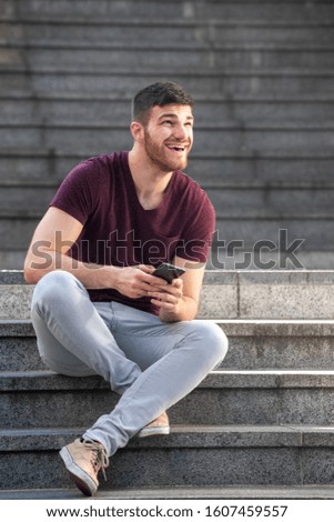 Portrait young man sitting on steps outside with cellphone