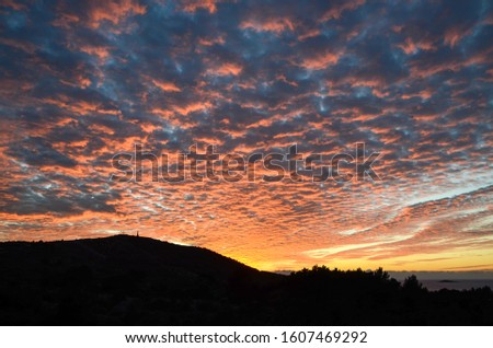 Beautiful sunset at coast. Red, orange and yellow clouds. Dramatic burning clouds in the evening sky. The setting sun with and silhouette of mountains. Landscape. Colorful and vibrant sunset skies.