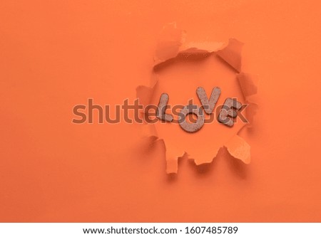 The word love in a torn hole of orange background. Top view