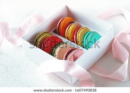 Multicolored macaroons in a white box on a white background with pink ribbon