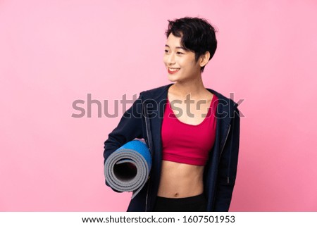 Young sport Asian woman over isolated pink background with a mat and smiling