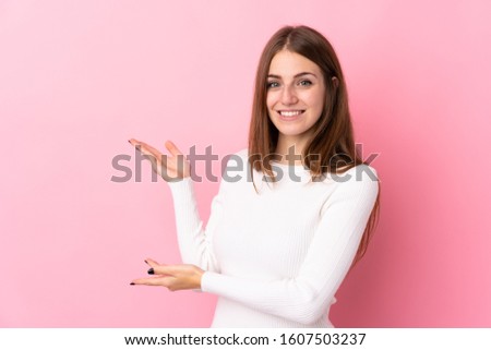 Young woman over isolated pink background extending hands to the side for inviting to come