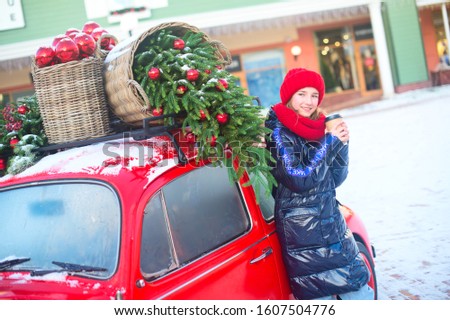Happy young model girl with cup of hot beverage in hands stand near decorated red car ready for shoping in europe outlet. Strape on her coat "Make it snow"