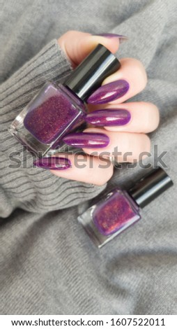 Female hand with long nails and a bottle of purple lilac color nail polish