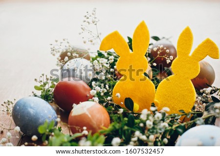 Happy Easter. Stylish easter eggs, yellow bunny in nest of spring flowers on rustic wooden table, space for text. Natural dyed easter eggs and rabbit decorations on wooden background