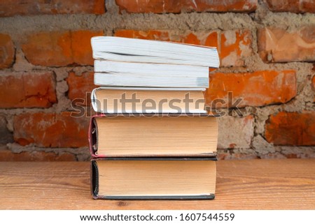 Books on a wooden shelf on a background of a brick wall.
