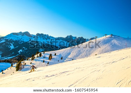 Winter landscape in Dolomites mountains, Italy, ski slope with snowboarder in Val di Fassa with mountain range in background, Vigo di Fassa area