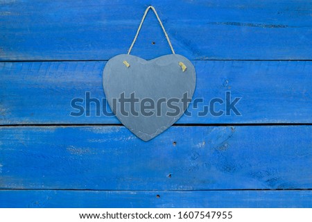 Blank slate heart sign hanging by rope on antique rustic blue wood door; Valentines Day holiday and love concept background with painted copy space