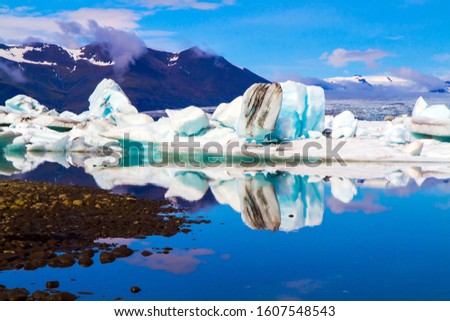 White and blue icebergs and ice floes reflected in the water. Iceland. The lagoon Jokulsaurloun.  The ice is covered in volcanic ash. The concept of northern and photo tourism