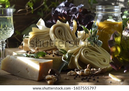 Fresh pappardelle ribbons on a cutting board with a chunk of parmesan, black peppercorns and sage.  Jar of pumpkin sauce and lettuce greens in background.