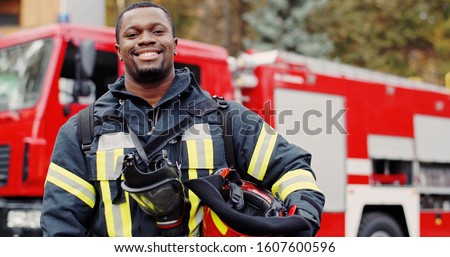 Firefighter portrait on duty. Photo of happy fireman with gas mask and helmet near fire engine Royalty-Free Stock Photo #1607600596