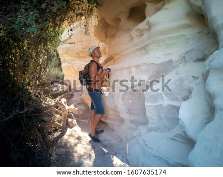 Young man with a hat taking picture with camera of white walls in Avakas Gorge, canyon in Akamas, Cyprus, not far from Paphos. Hanging Stone. Cyprus Landmark. Filtered image. Vacation concept.