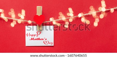Happy Mother's Day background banner - White paper note hang on wooden clothes pegs with wooden hearts on a string isolated on red paper texture and bokeh lights, with space for text