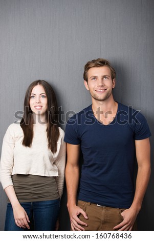 Attractive thoughtful young couple standing side by side against a clean blackboard with copyspace staring up into the air