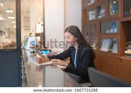 Welcome to the hotel,Happy young Asian woman hotel receptionist worker smiling standing,she taking telephone call at a Modern luxury reception counter waiting for guests getting key card in hotel