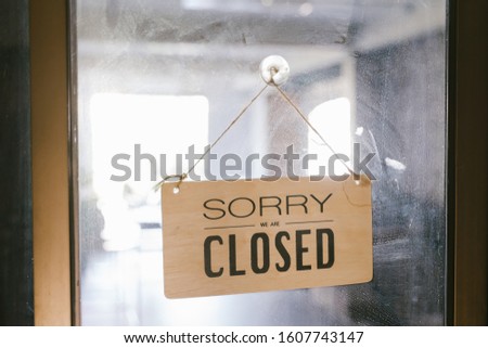 Through glass of stylish wooden closed sign board on door of restaurant at city street
