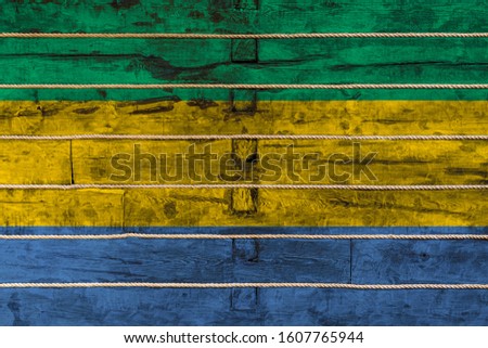 National flag  of Gabon
on a wooden wall background. The concept of national pride and a symbol of the country. Flags painted on a wooden fence with a rope