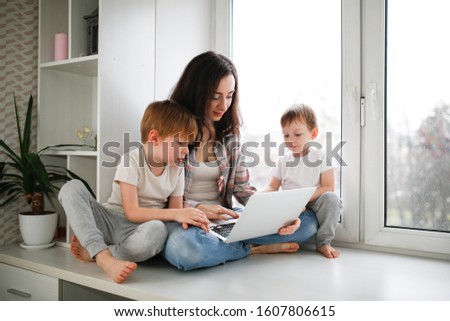 Mom works on a laptop on window sill, mother with children online shopping. children and mom look at laptop. Authentic lifestyle and sincere real family. Concept online shopping and mother freelancer
