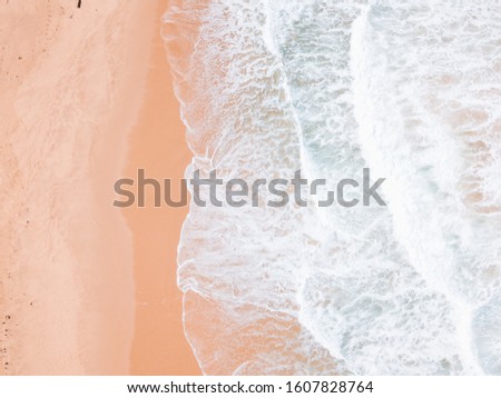 Top view of sandy beach with foam, sand texture, beautiful waves, aerial drone shot.