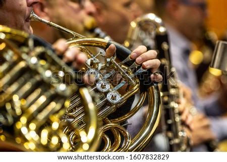 Young woman playing on french horn during philharmonic concert