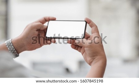 Cropped shot of professional businessman holding horizontal blank screen smartphone with blurred office room background