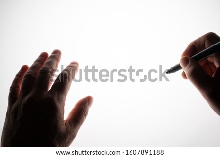 one hand writes with the pen on a backlit surface