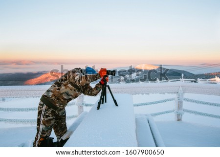 Photographer with camera on tripod at sunset during frozen winter day