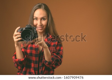 Studio shot of young beautiful woman with camera against brown background