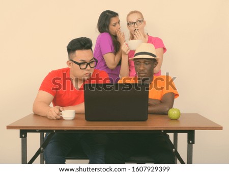 Diverse multi ethnic group of friends using laptop with friends whispering at the back
